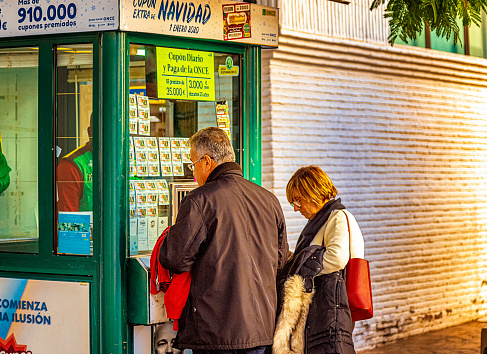 Two adults buying lottery tickets by a small booth in Nerja, Andalusia, Spain. Lottery is a big thing in Spain, especially around Christmas where nearly everybody will invest some money.