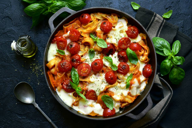 Pasta casserole with tomatoes and mozzarella cheese in a cast iron pan Pasta casserole with tomatoes and mozzarella cheese in a cast iron pan on a dark slate, stone or concrete background. Top view with copy space. sauce photos stock pictures, royalty-free photos & images