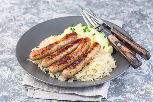 Roasted nuremberg sausages served with sour cabbage and mashed potatoes, on a gray plate, horizontal