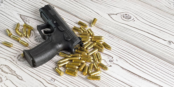 istock Black metal gun and brass yellow bullets scattered on white boards, space for text right side 1190040486