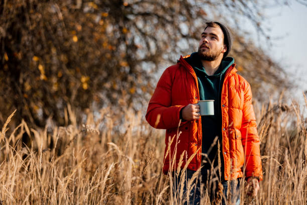 Style man in down jacket with cup of coffee at rural autumn outdoor stock photo