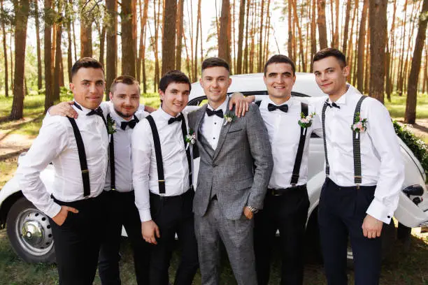 Group wedding photography. Elegant groom in grey suit with groomsmen with black bow ties and suspender at wedding day