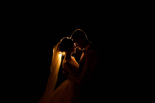 Creative idea of wedding photography at night. Silhouette of a bride and groom illuminated by a lights Creative idea of wedding photography at night. Silhouette of a bride and groom illuminated by a lights veil photos stock pictures, royalty-free photos & images