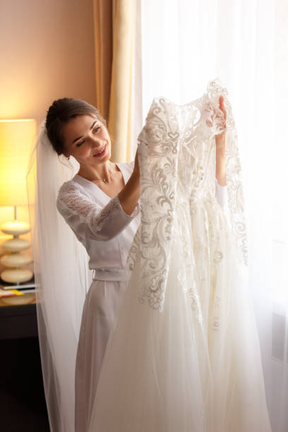 istock Bride holding white wedding dress with lace, embroidery. Bride getting ready 1190043655
