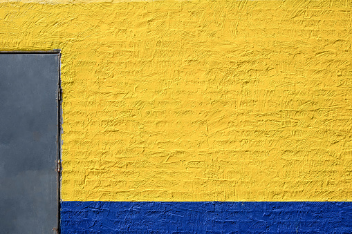 Painted yellow and blue brick wall with metal door and copy space