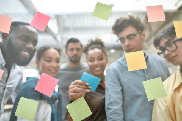 istock Creative team at work. Group of young and positive coworkers putting colorful sticky notes on a glass window while standing in the modern office 1190052311