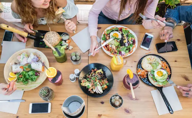 Photo of Top view of young people eating brunch and drinking smoothie bowl at  vintage bar - Students having a lunch and chatting in trendy restaurant - Food trends concept - Focus on center tab