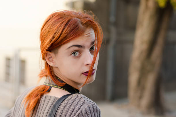 Young woman with long red hair stares ahead with an expression of uncertainty or anxiety.