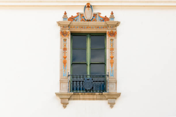 istock Beautiful ornate window with decorative trim with yellow and blue design elements in a white plaster wall of an old building 1190069207