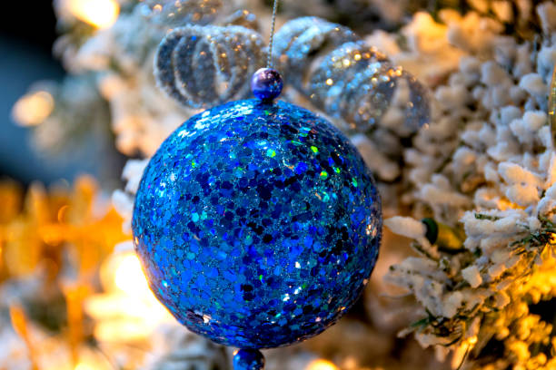 Blue sequined Christmas ball hanging from an illuminated, flocked Christmas tree is a welcoming sight for a family that is home for the holidays.