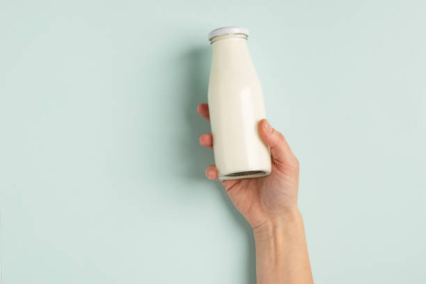 Female hand holds milk or white milk drink in a glass bottle on white background. Healthy eating concept. Flat layout . Female hand holds milk or white milk drink in a glass bottle on a white background. Healthy eating concept. Flat layout top view. Copy space. Horizontal frame probiotic photos stock pictures, royalty-free photos & images