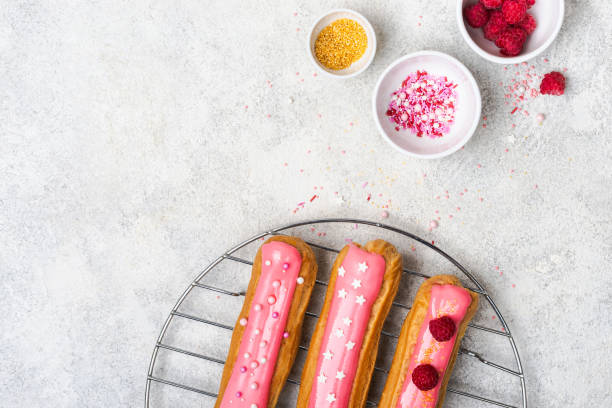 istock Delicious eclairs with pink glaze, raspberry and sugar sprinkles on gray background, copy space 1190086419