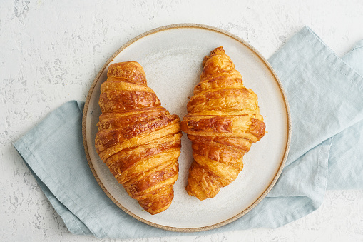 Two delicious croissants on a plate and a hot drink in a mug. Morning French breakfast with fresh pastries. Light gray background. Long width banner