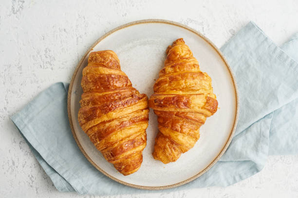 two delicious croissants on plate and hot drink in mug. morning french breakfast with fresh pastries. light gray background. long width banner - cooked bread food cup imagens e fotografias de stock