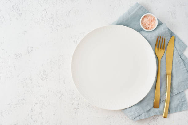 istock Clean empty white plate, fork and knife on white stone table, copy space, mock up, top view. Concept for menu 1190095851
