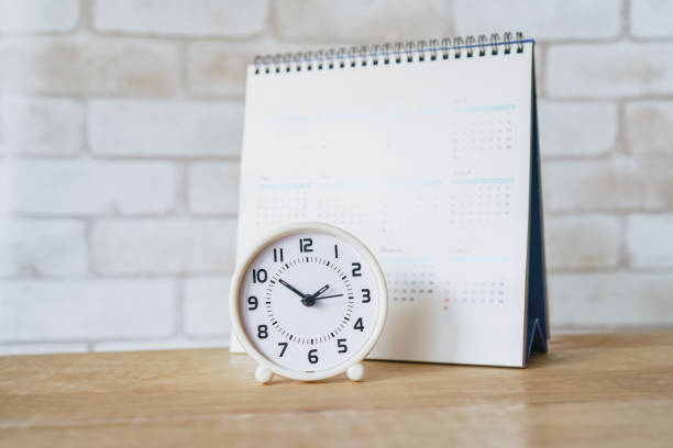 istock white analog clock with blurred calendar on wooden table 1190097942