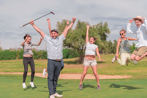 A group of young people jumping happily on a golf course in the summer. Concept of a day of relaxation and leisure. Horizontal image