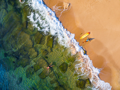 Aerial view of a surfer girl resting on a beach and man swimming in the sea