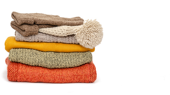 A stack of folded knitted warm women sweaters, hat and gloves on a white background. Time to keep warm. Season of warm clothes. Close-up. Copy space