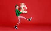 cheerful funny child in Christmas elf costume with gifts on   red background