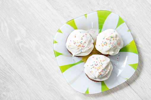Tasty cupcakes in the plate on a white wooden table. Sweet beautiful cake for birthday greeting card or party invitation.