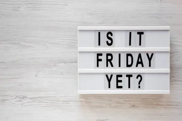 'Is it friday yet ?' words on a lightbox on a white wooden background, top view. Overhead, from above, flat lay. Copy space.