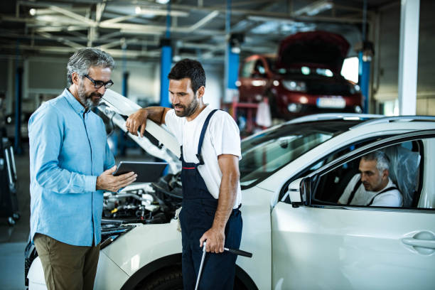 gerente sonriente y mecánico de automóviles trabajando en tabletas digitales en un taller de reparación. - auto repair shop mechanic digital tablet customer fotografías e imágenes de stock