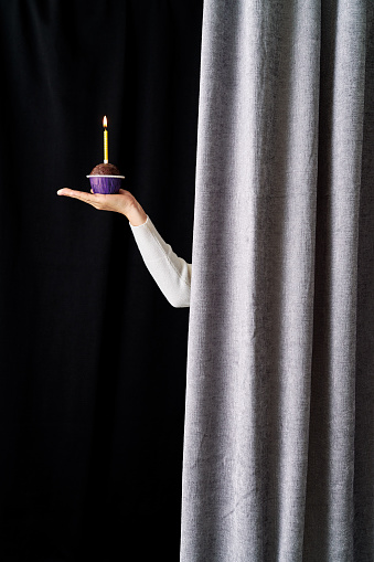 Women hand showing cake with candle behind of curtain.