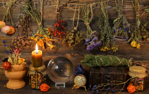 Still life with dry herbs, crystal ball, bottle and burning candle on witch table. stock photo