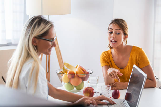 professionelle ernährungsberaterin trifft einen patienten im büro. junge lächelnde ernährungswissenschaftlerin im sprechzimmer. ernährungsberater schreibtisch mit gesunden früchten und maßband. - document healthcare and medicine stethoscope history stock-fotos und bilder