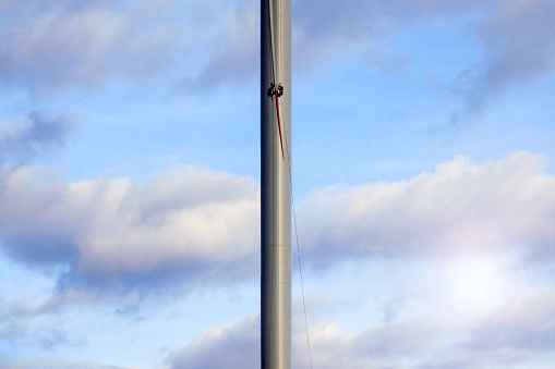 Rope access technician doing inspection of blade on wind turbine high up with beautiful clouds behind