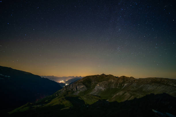 many stars on night sky high up in mountains lighted village down in mountain valley