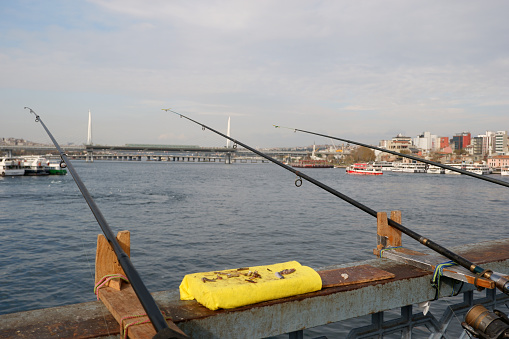 Three fishing rods and fish baits of an amateur fisherman by the Golden Horn Istanbul on Galata bridge. Halic bridge is visiable on the blurred backround.