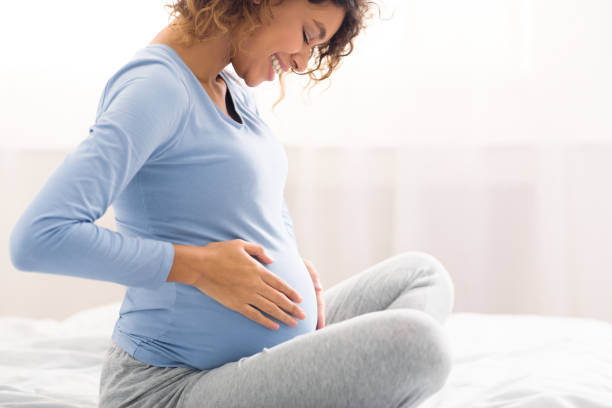 Happy expectant woman touching belly, side view Happy expectant woman touching belly, enjoying unborn baby pushings in bed, side view pregnant stock pictures, royalty-free photos & images