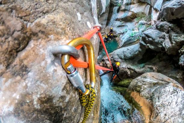 An adventurist making an abseil down a small waterfall while canyoning with his group An adventurist making an abseil down a small waterfall while canyoning with his group. carabiner stock pictures, royalty-free photos & images