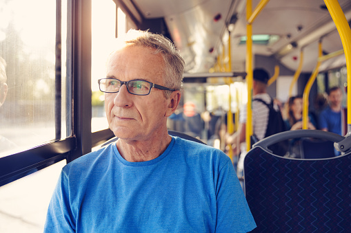 Thoughtful senior man sitting in public transport. Male is looking through window while traveling in bus. He is wearing eyeglasses.