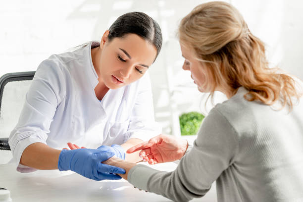 attractive dermatologist in white coat examining skin of patient in clinic stock photo