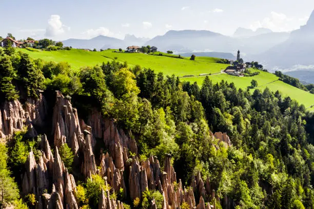 The Earth Pyramids of the Renon near village Mittelberg (Monte di Mezzo) in South-Tirol, Italy, with the church St. Nikolaus (San Nicolo). In the background the Dolomite Alps. South-Tirol is bilingual: German and Italian. Thus the two names for locations and mountains.