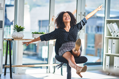 Full length shot of an attractive young businesswoman sitting alone in her office and feeling playful during a break