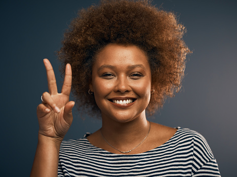 Studio portrait of an attractive young woman showing the peace sign while standing against a grey background