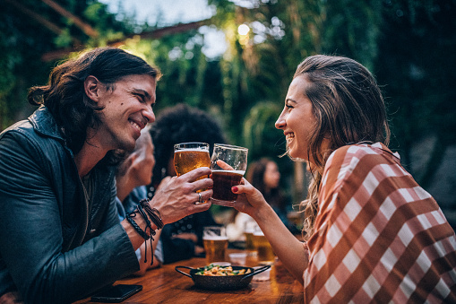 Man and woman, couple sitting outdoors in pub together, drinking beer.