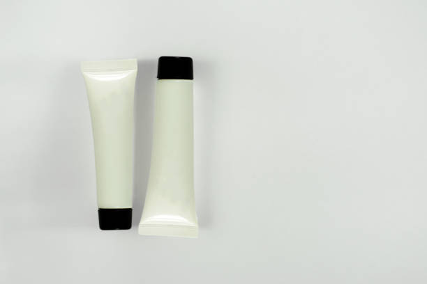 istock Two blank white tubes with black top caps on light background with shadows. Closeup mockup of cosmetics containers for cream, paste, lotion, gel, shampoo and others 1190141598