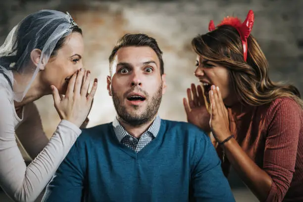 Shocked businessman sitting in the office while angel and devil are whispering him something.