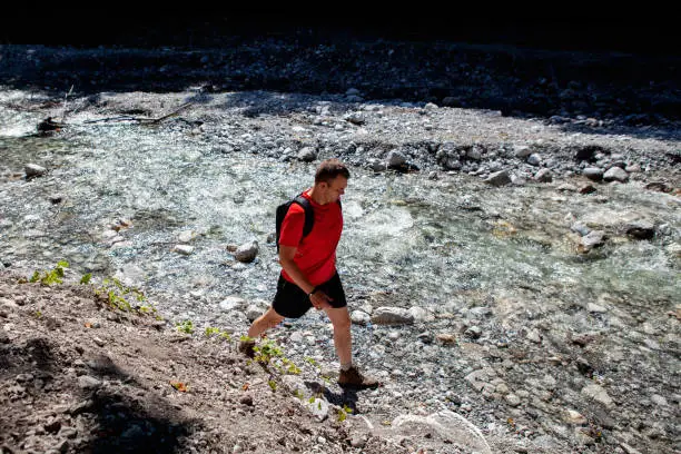 Lofer, Austria - August 11, 2019: high angle view of a man walking briskly next to a rocky mountain river on a hot summer day in Austria