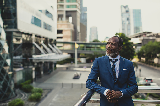 Portrait of elegant African businessman standing on a balcony at modern business district at the city.