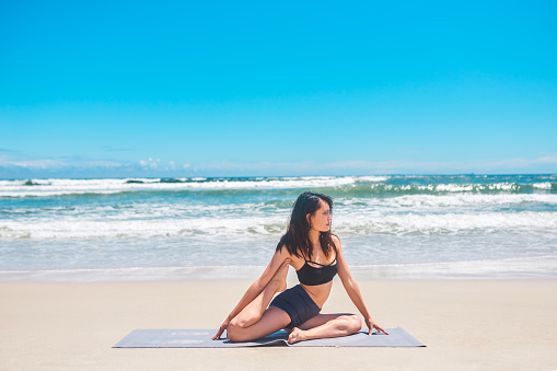 Shot of a young woman practising yoga at the beach