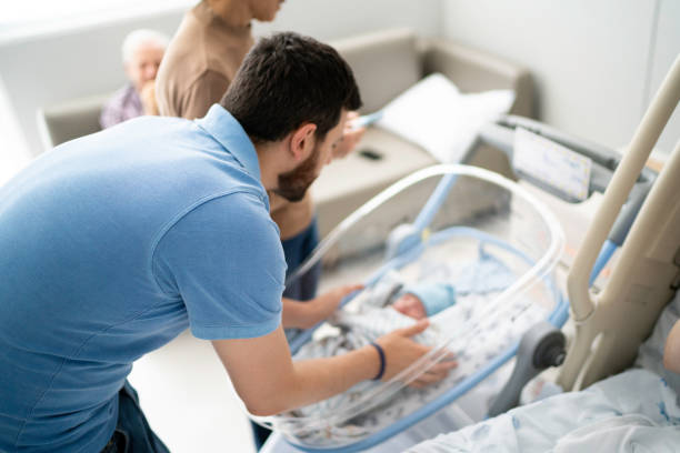 familie mit blick auf neugeborene auf der krankenstation - hispanic male stock-fotos und bilder