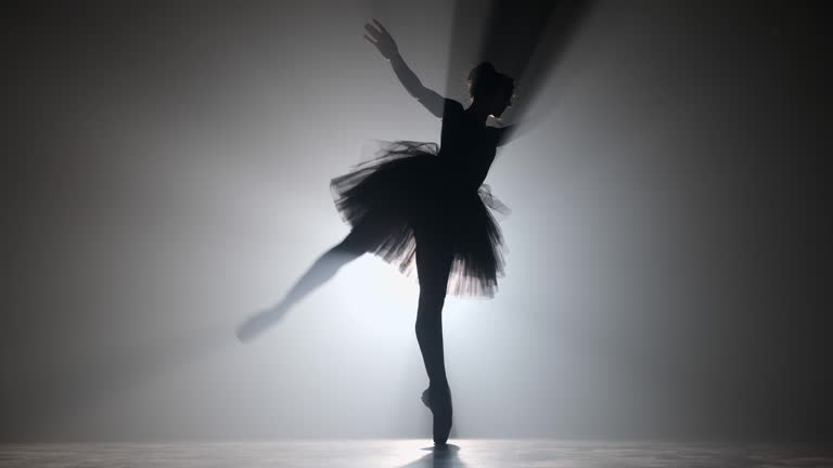 Professional ballerina dancing ballet in spotlights smoke on big stage. Beautiful young girl wearing black tutu dress on floodlights background. Black and white. 4k