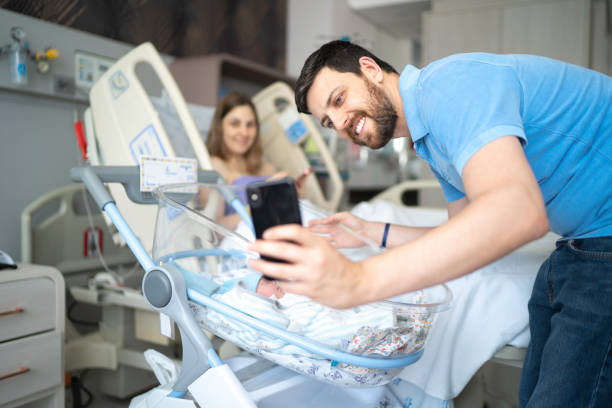 glücklicher vater macht ein selfie von seinem neugeborenen und seiner frau im krankenhaus - phone cradle stock-fotos und bilder