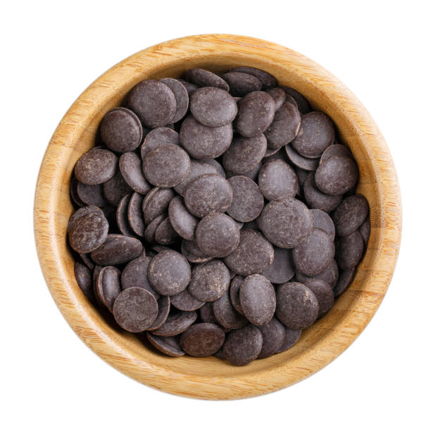 istock Dark unsweetened chocolate chips in wooden bowl isolated on white. Top view. 1190159480